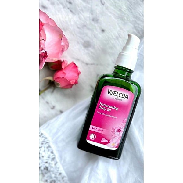 Harmonising Body Oil Wild Rose next to roses.