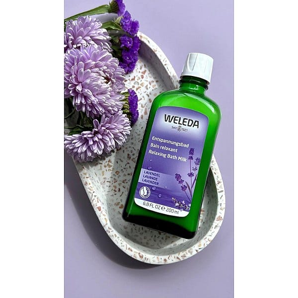 Relaxing Bath Milk Lavender on a marble plate next to purple flowers.