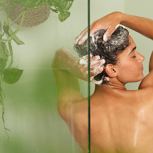 Woman in shower showing her back, while washing her hair.
